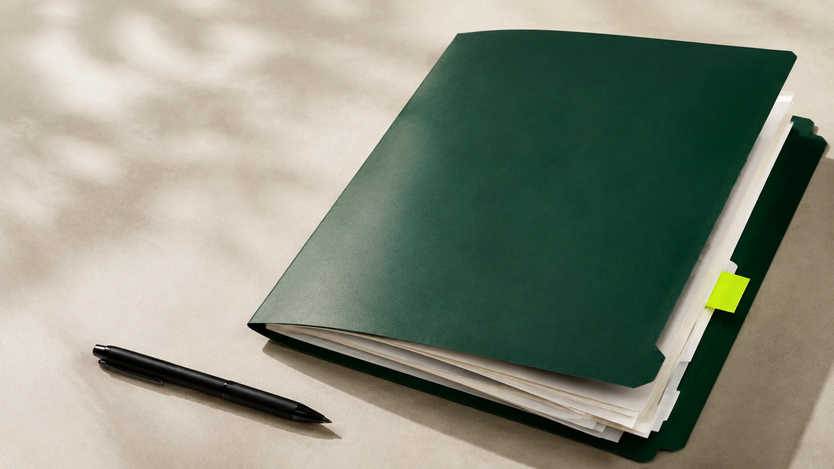 A deep green folder with neatly stacked documents, a black pen, and a lime page marker on a pale desk.